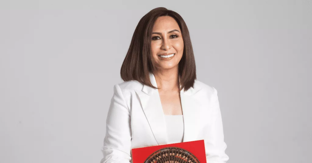 Woman in a white suit holding a red folder, smiling against a plain background.